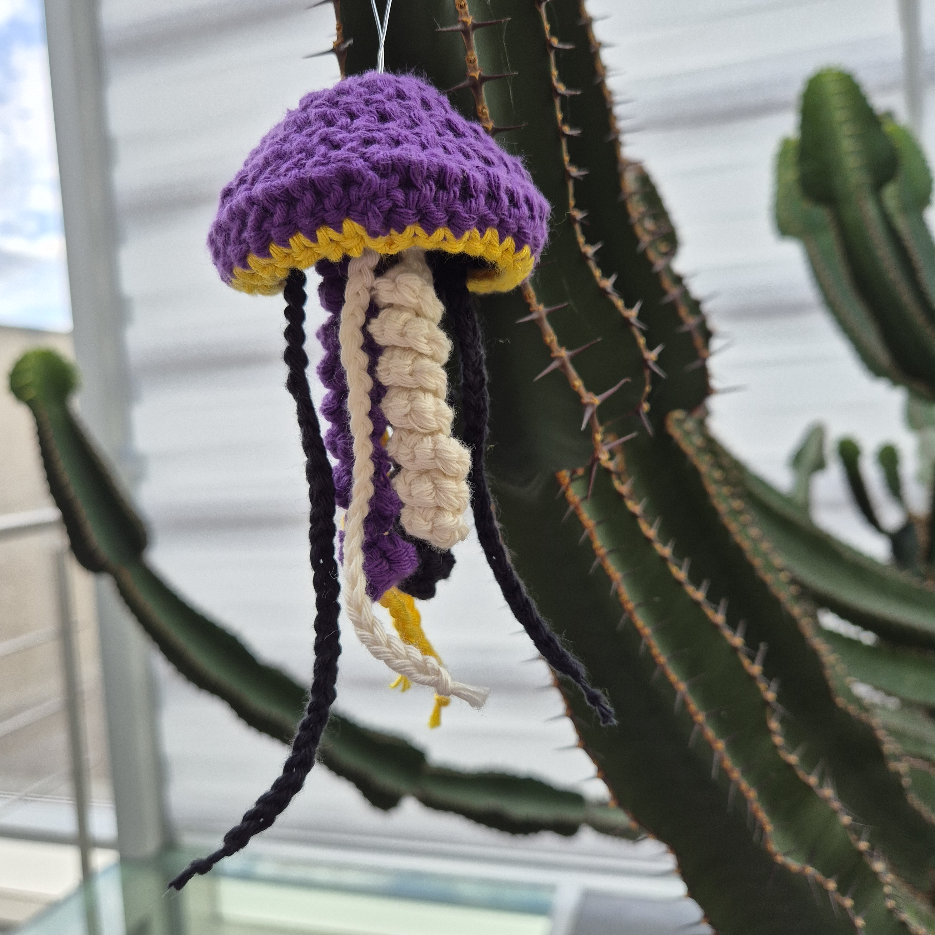 Photo of a crocheted jellyfish hanging from the arm of a cactus