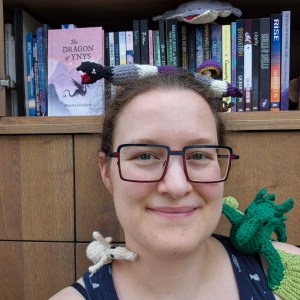 Photo of Minerva surrounded by crocheted Sea Creatures and with xyr books in the background.