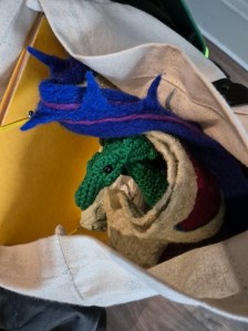 Photo of a crocheted dragon and a felted dragon wing sticking out of a tote bag.
