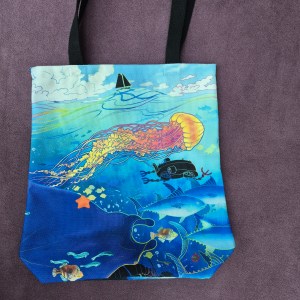 Photo of a BE THE SEA totebag lying flat on a purple background.